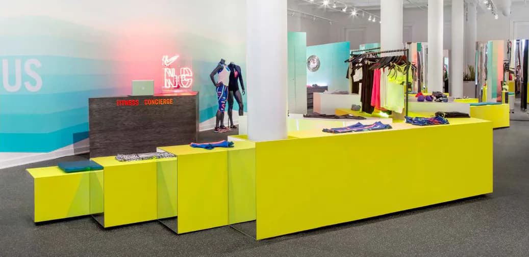 Bright retail interior with modular yellow counter display units, turquoise and pink accent walls, clothing racks, and polished concrete flooring by Erik Tietz.
