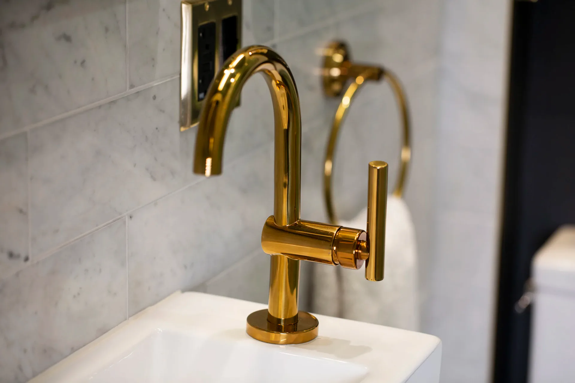 Polished brass single-spout faucet mounted on white marble countertop with subway tile backsplash, contemporary bathroom design by Erika Schmitt.