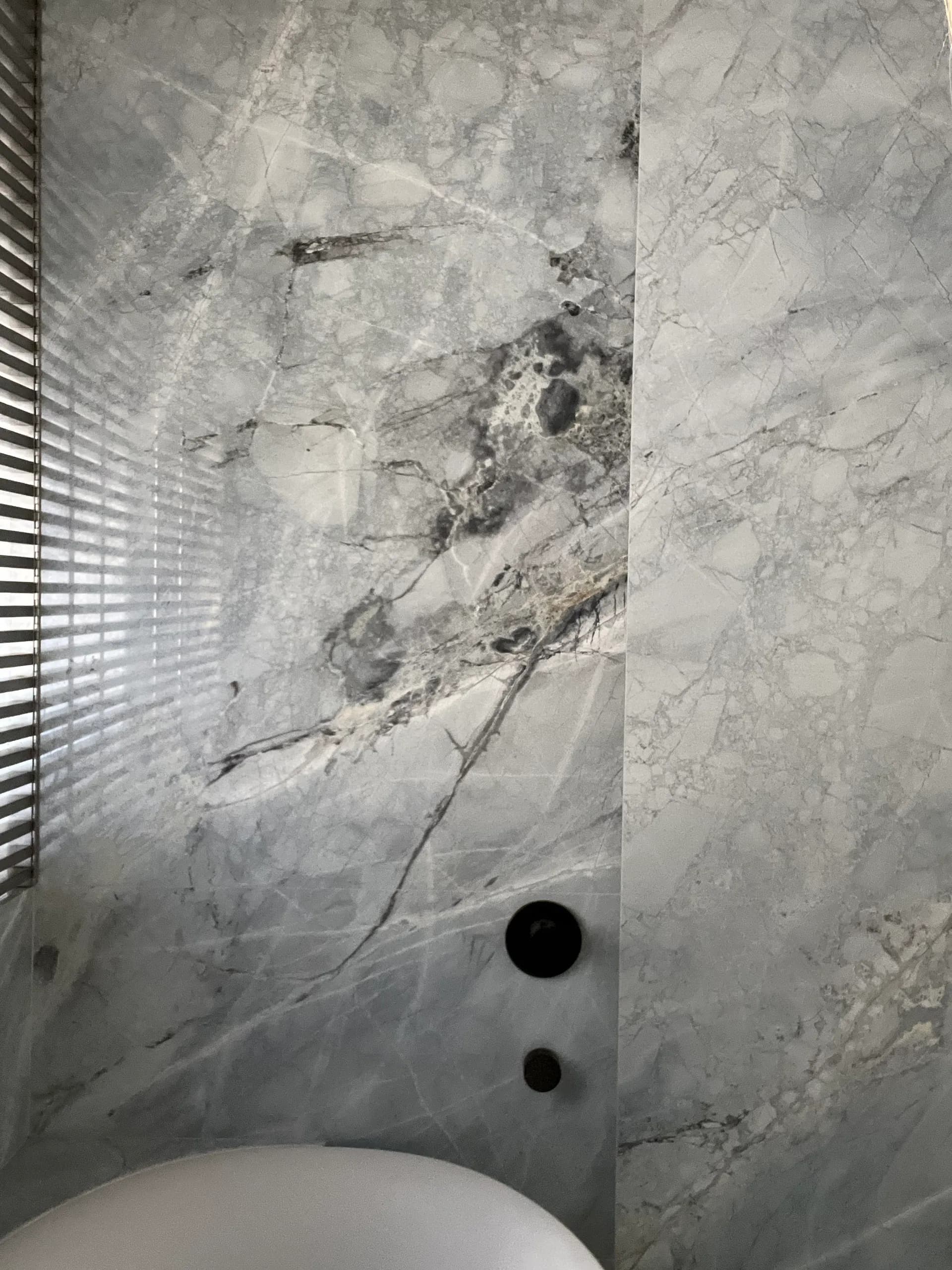 Marble bathroom with veining detail, white fixtures, and minimalist design by Erika Stahlman.