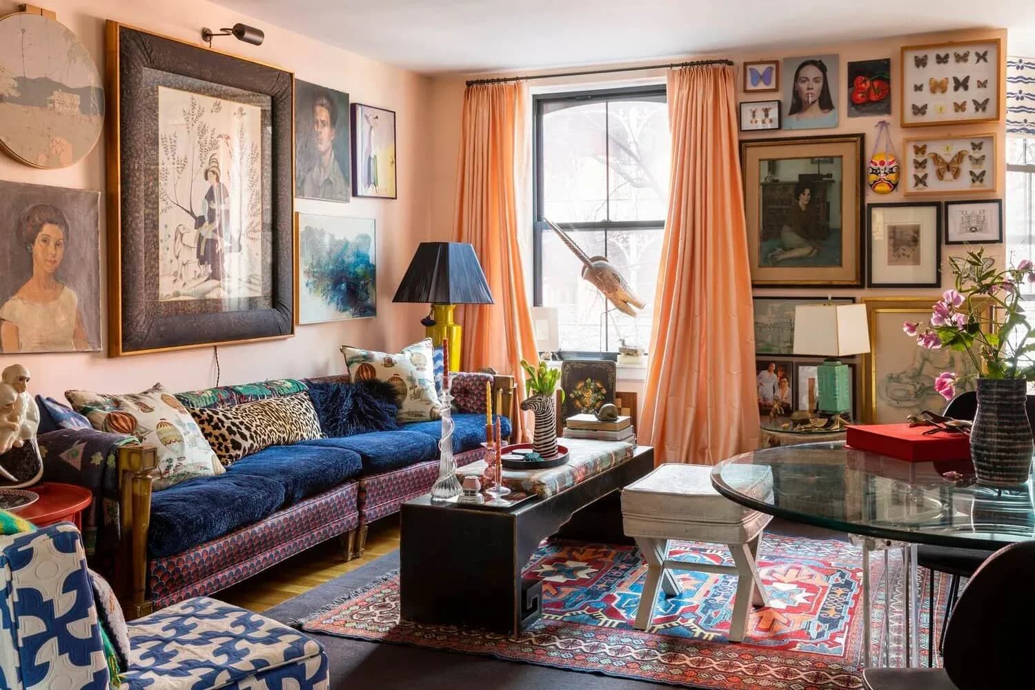 Eclectic living room with blue velvet sofa, gallery wall, colorful layered rugs, orange curtains, and vintage furnishings by Erin Fearins.