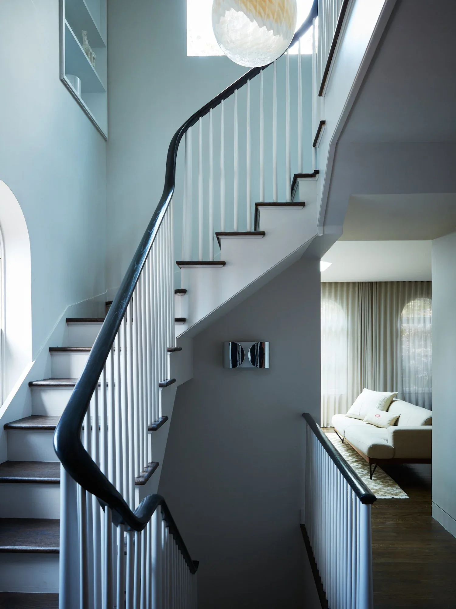 Sculptural black staircase with metal railing curves through light-filled multi-level interior, connecting bedroom with sitting area, by Erin Fearins.