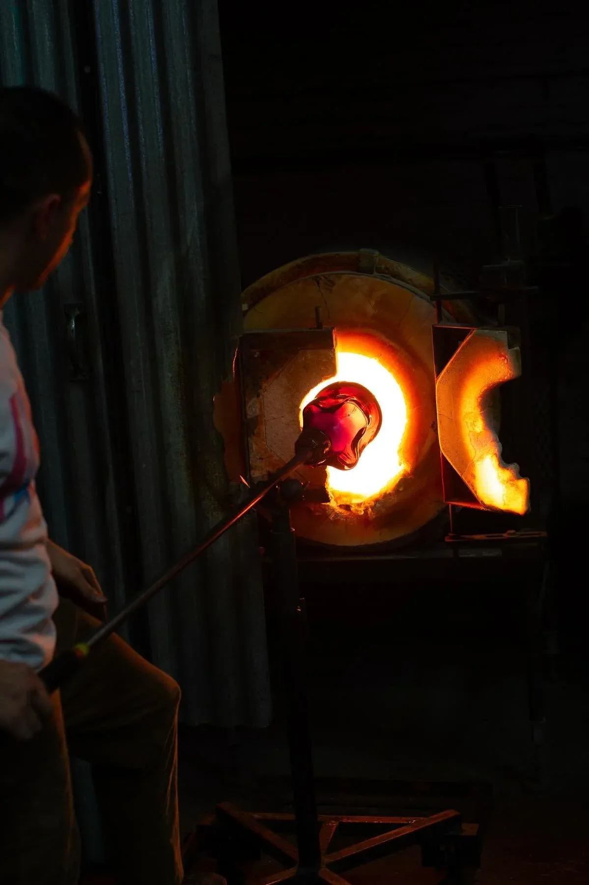 Industrial glass-blowing or metalworking installation with glowing orange furnace chambers and a craftsperson at work, showcasing thermal design by Esteban Salazar-Cucalon.