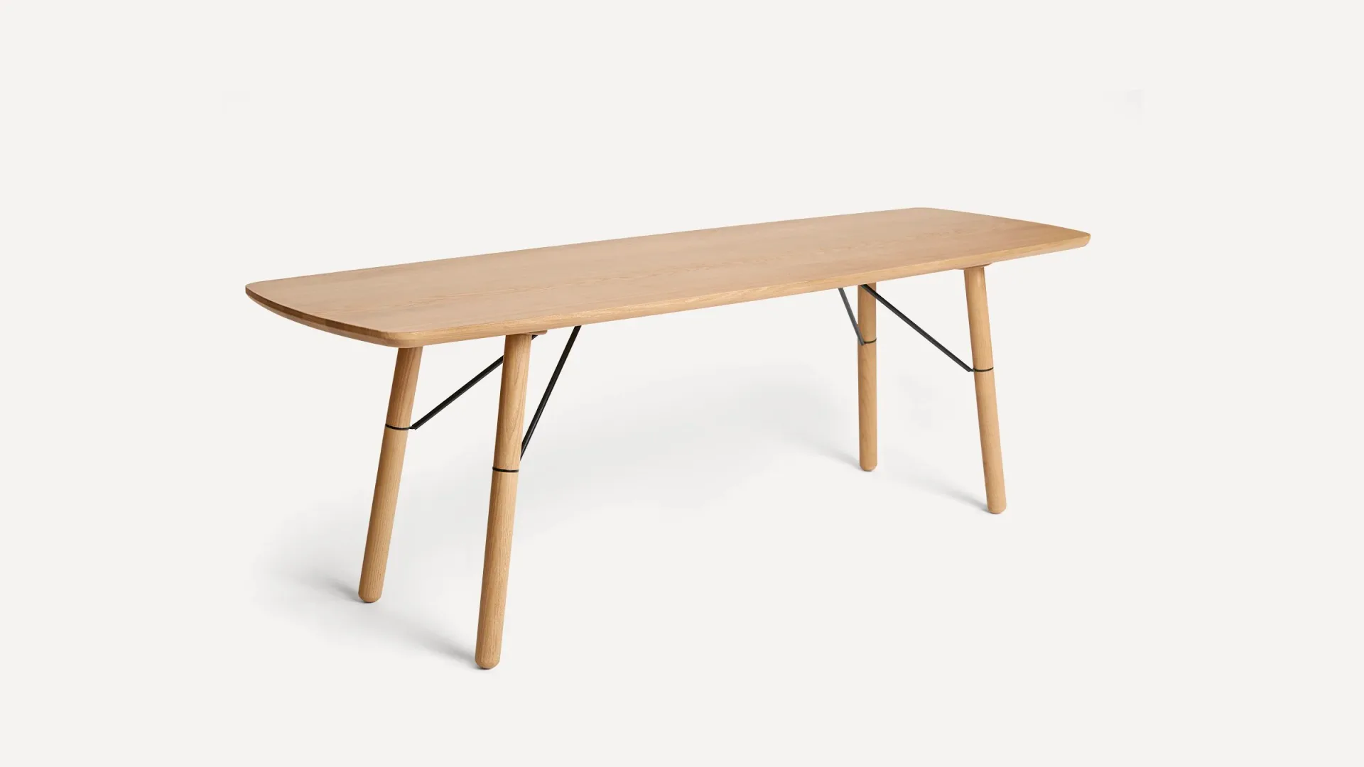 Light wood dining table with curved top and angled leg braces against neutral background by Evan Clabots.