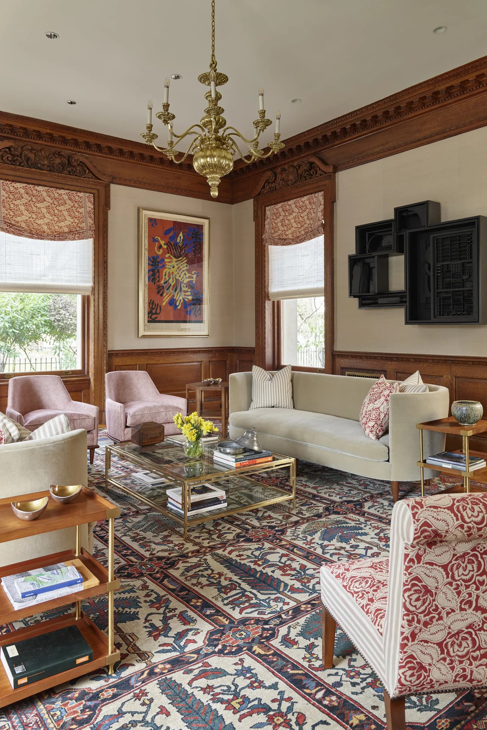 Traditional living room with wood paneling, brass chandelier, patterned area rug, pink velvet chairs, and framed artwork, designed by Eve Wildrick.