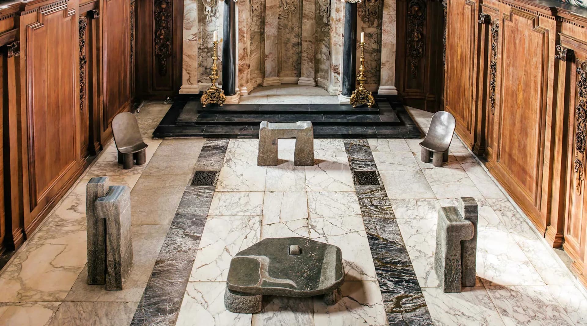 A marble-floored gallery space with geometric stone inlay patterns, classical columns, and sculptural bronze vessels arranged symmetrically by Faye Toogood.