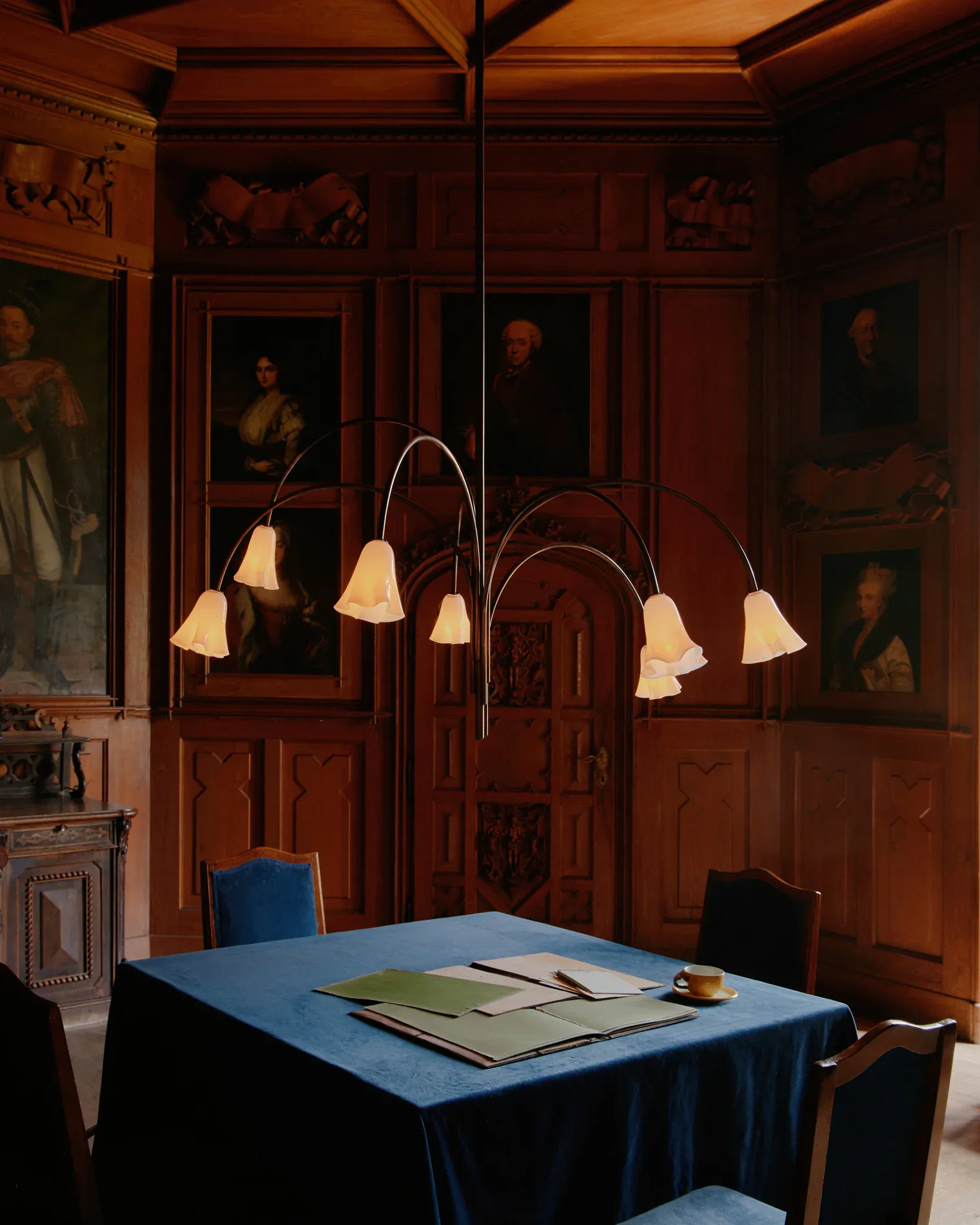 Warm wood-paneled dining room with blue tablecloth, portrait gallery wall, and curved arc floor lamp by Felicia Hung.