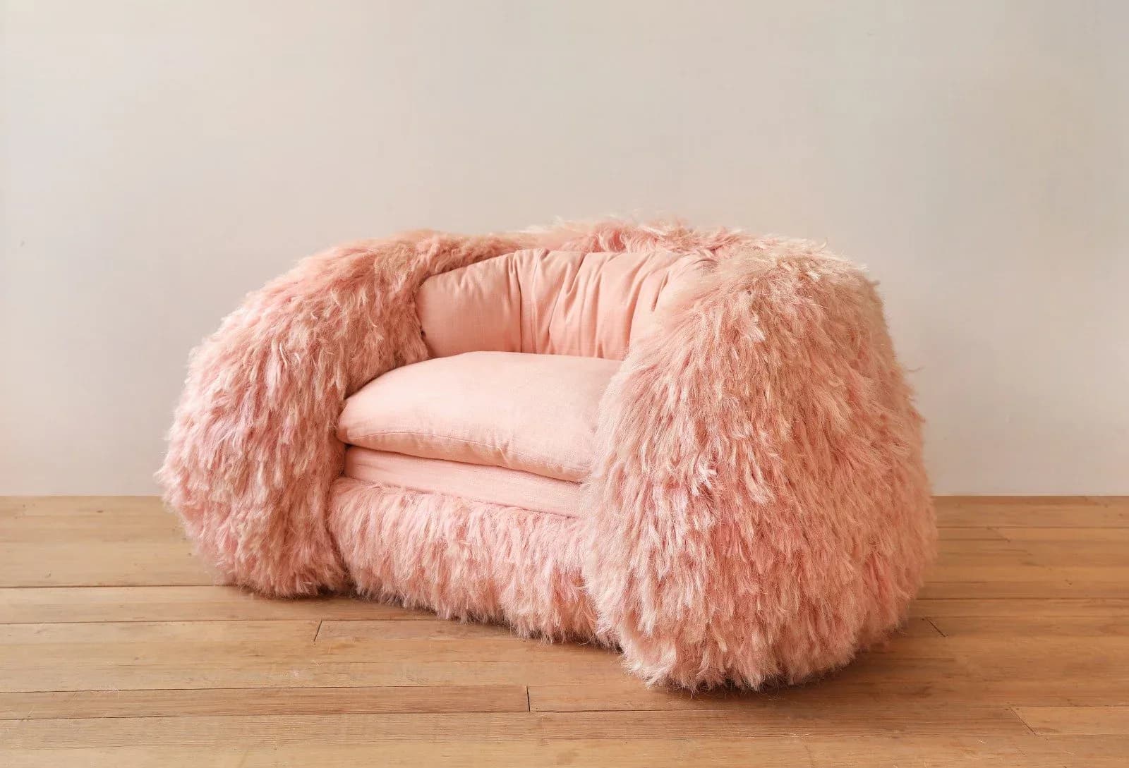 Pink faux-fur upholstered armchair with cushioned seat on wooden floor by Fernando Laposse.