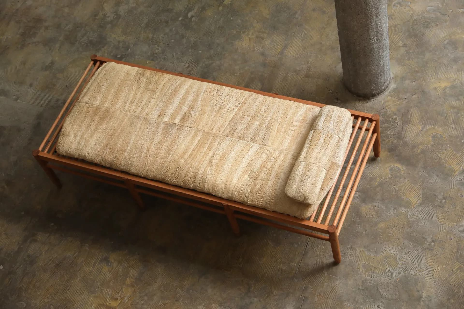 Wooden bench with woven natural fiber cushioning and tapered legs on concrete floor by Fernando Laposse.