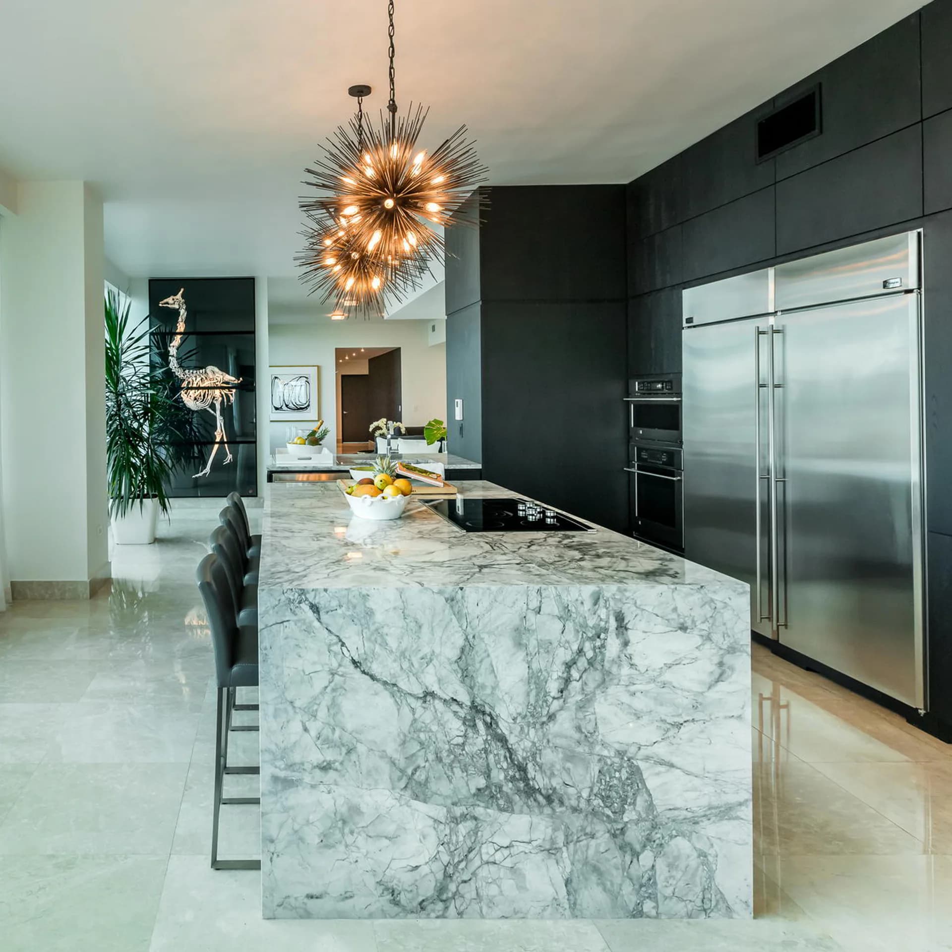 Modern kitchen with marble waterfall island, black cabinetry, stainless steel appliances, and brass sunburst pendant light by Fernando Rodriguez.