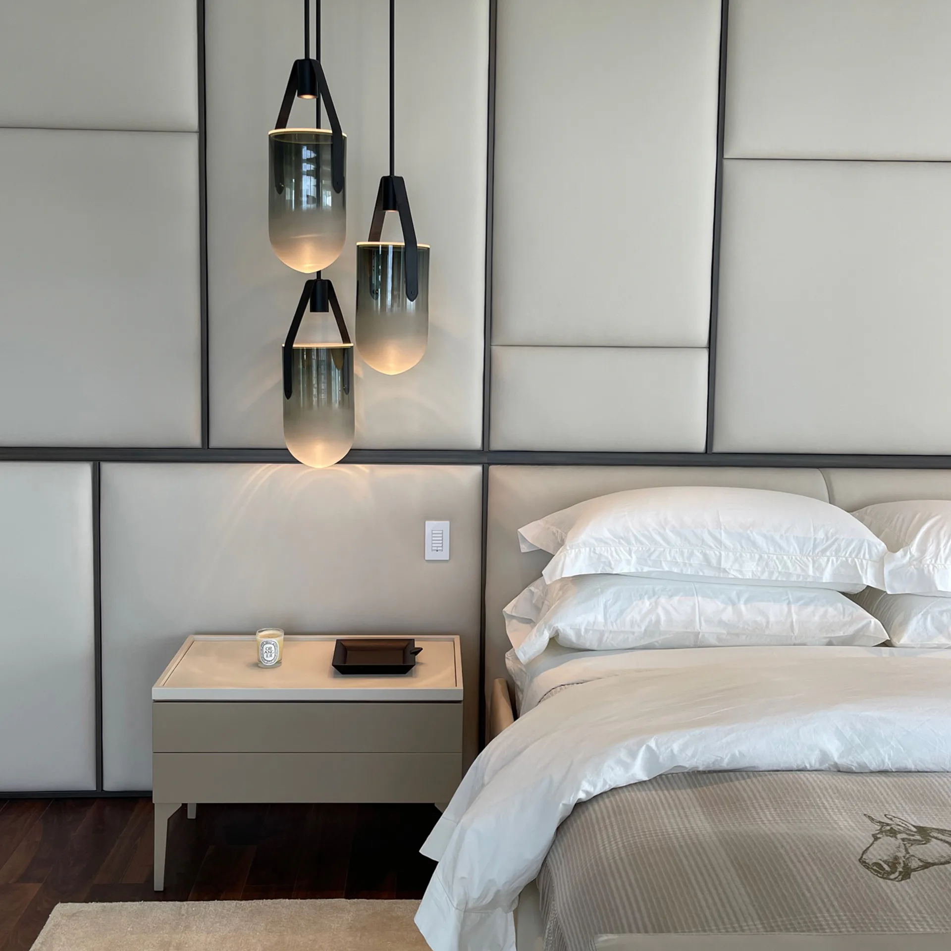 Modern bedroom interior with minimalist aesthetic featuring a bed with white linens, floating nightstand, and three pendant lights with black frames and frosted glass shades by Fernando Rodriguez.