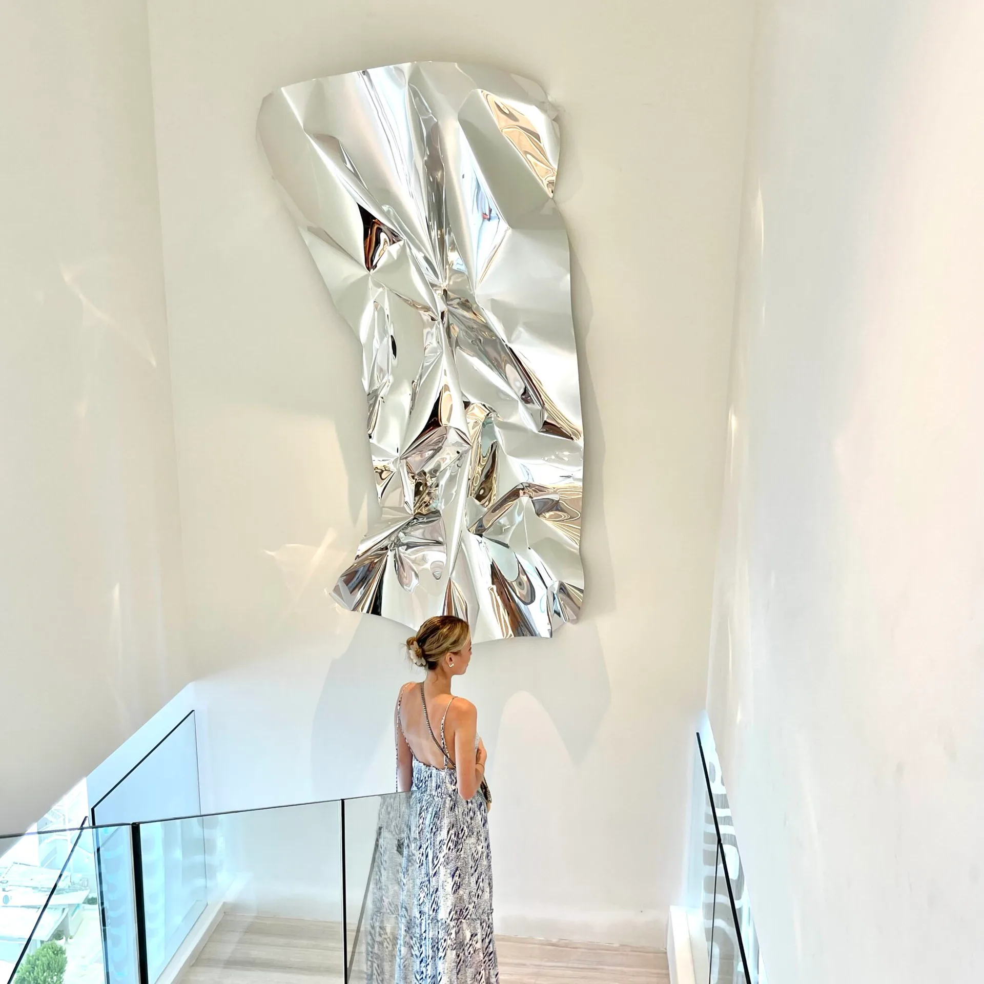 Modern interior with a woman viewing a large sculptural metallic wall installation in white gallery space by Fernando Rodriguez.