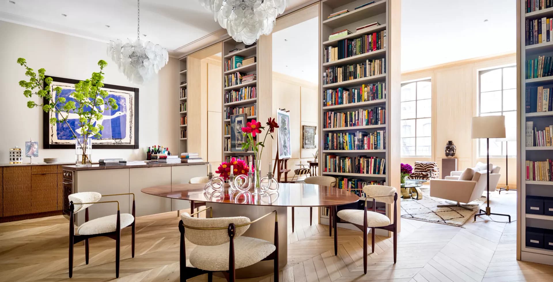 Contemporary living room with floor-to-ceiling bookshelves, round dining table, mid-century chairs, and bright natural light by Fiona Mueller.