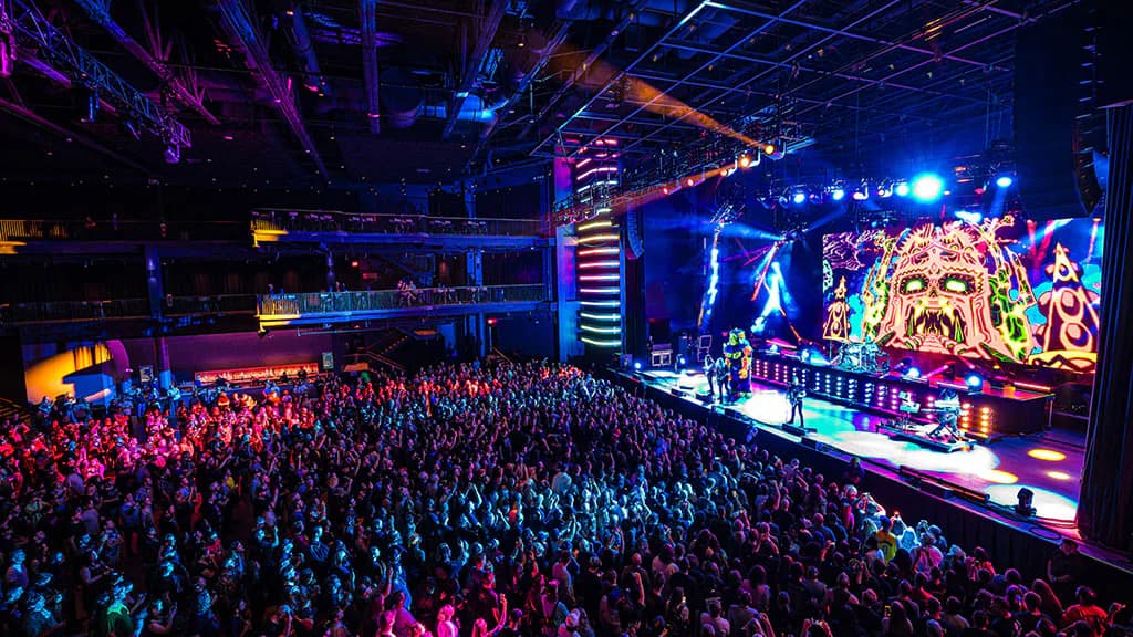 Large-scale concert venue interior with vibrant stage lighting, massive LED screens, and packed crowd, designed by Florence Lung.