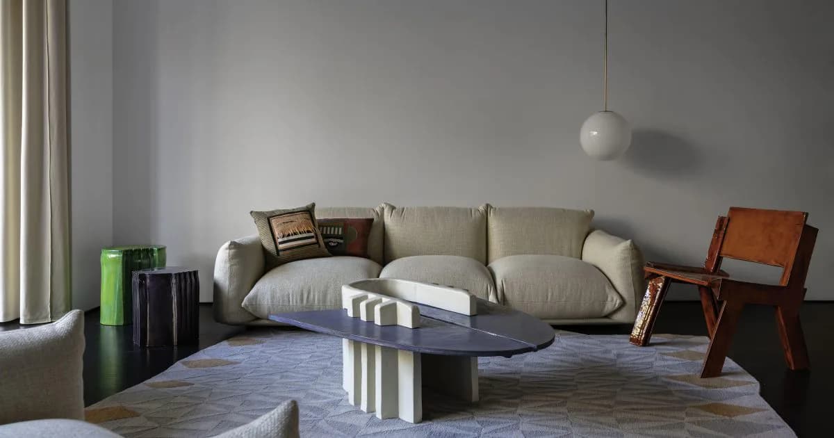 Modern minimalist living room with beige sectional sofa, black oval table, wood chairs, and geometric patterned flooring in muted tones by Floris Wubben.