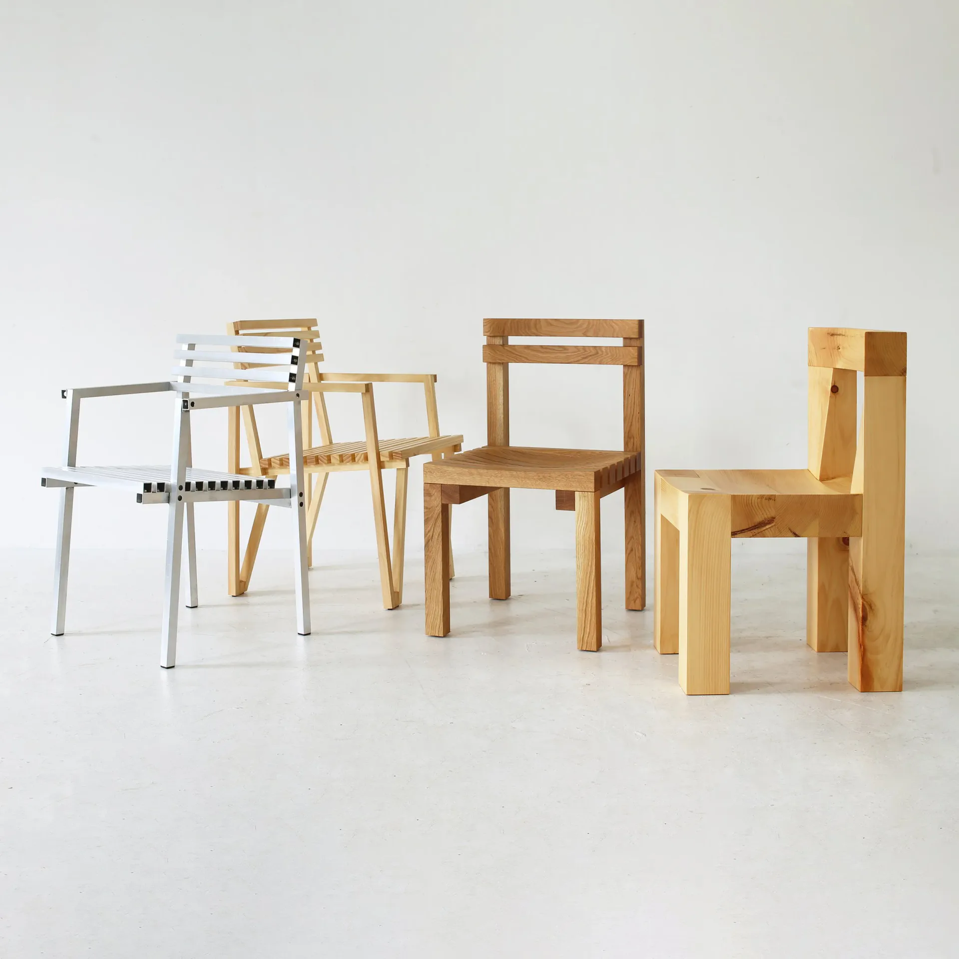 Collection of minimalist wooden and metal chairs in natural and light finishes arranged on a white background by Ford Bostwick.