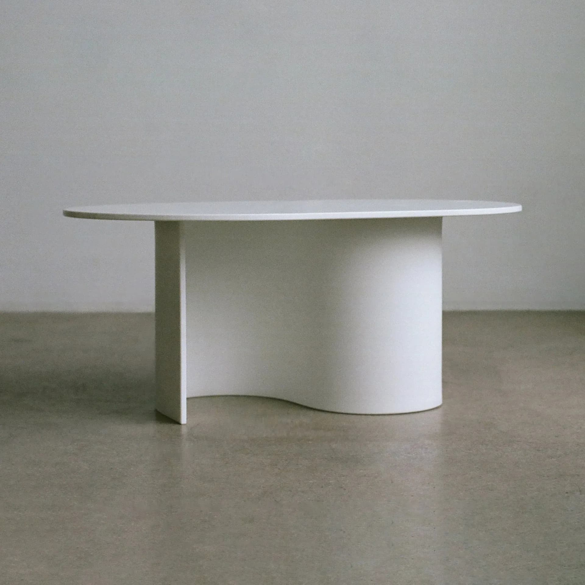 Minimalist table with curved white base and extended round top in neutral tones by Ford Bostwick.