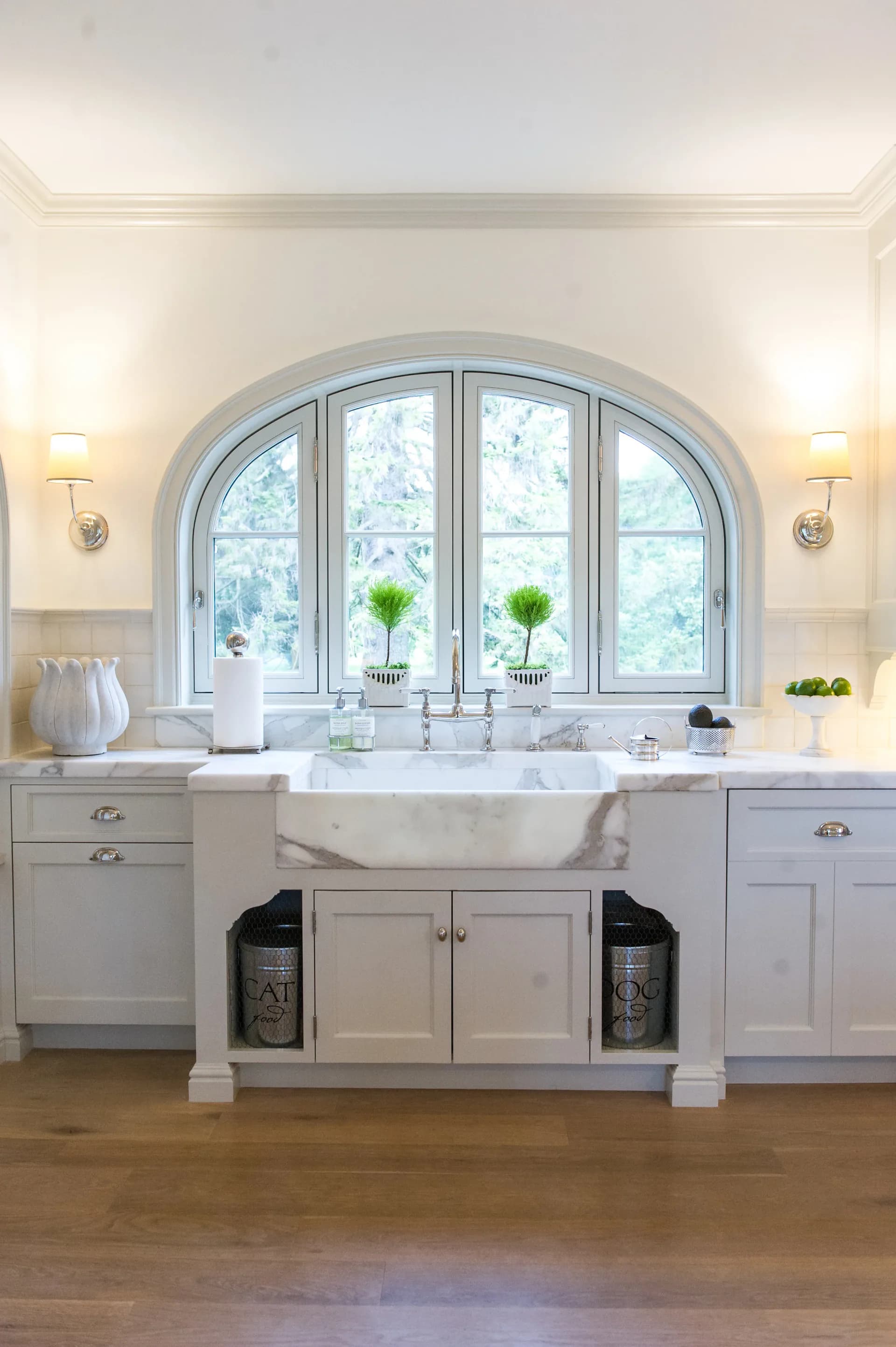 Elegant bathroom with arched window, white cabinetry, marble countertop, and freestanding sink by Fotini Levy.