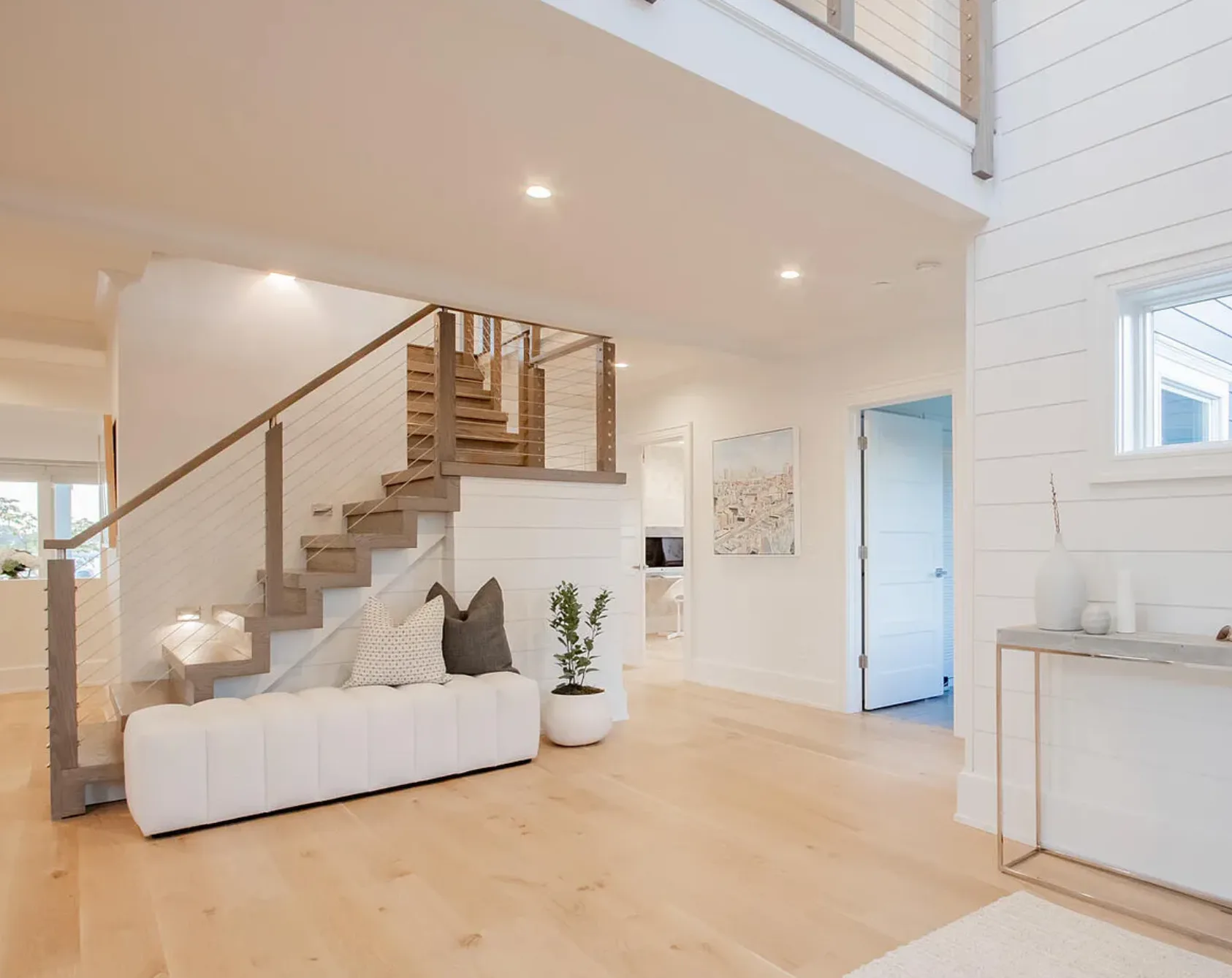 Bright minimalist loft interior with wooden staircase, white walls, light wood flooring, and modern furnishings by Fotini Levy.