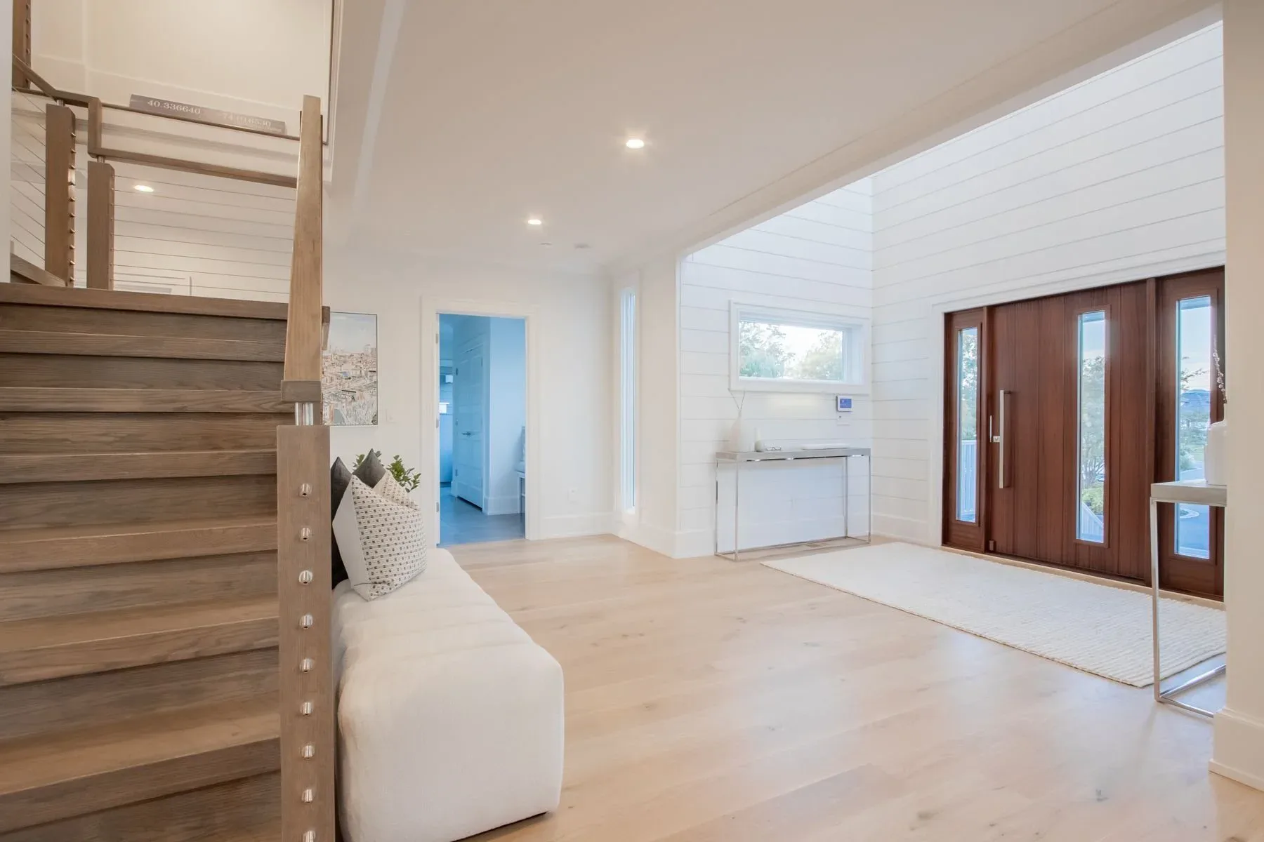Bright, minimalist interior with natural wood staircase, white walls, light oak flooring, and brown wooden doors, designed by Fotini Levy.