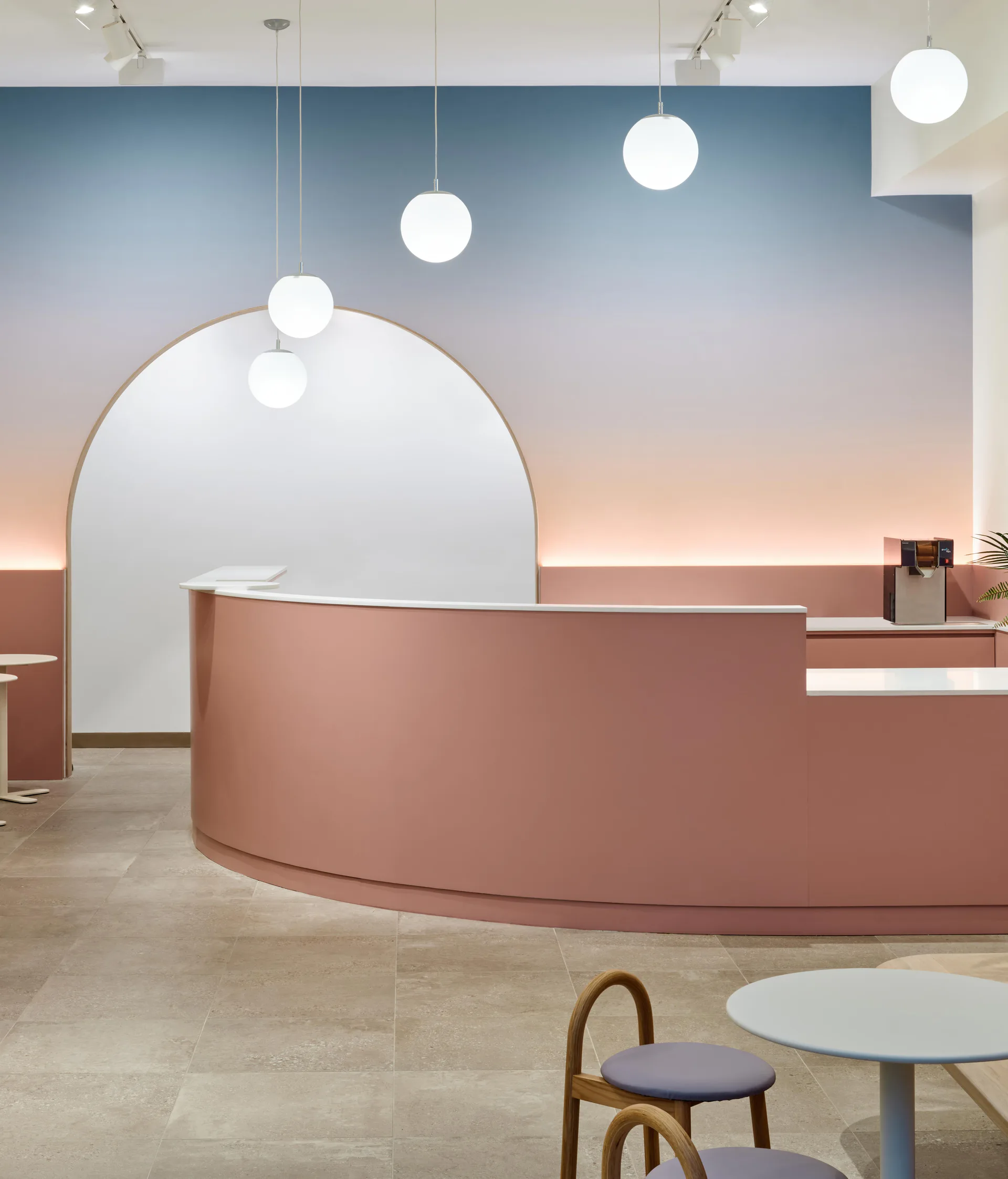 Modern reception area with curved mauve desk, arched white alcove, suspended globe pendant lights, and gradient sky-toned wall mural by Francesca Bastianini.