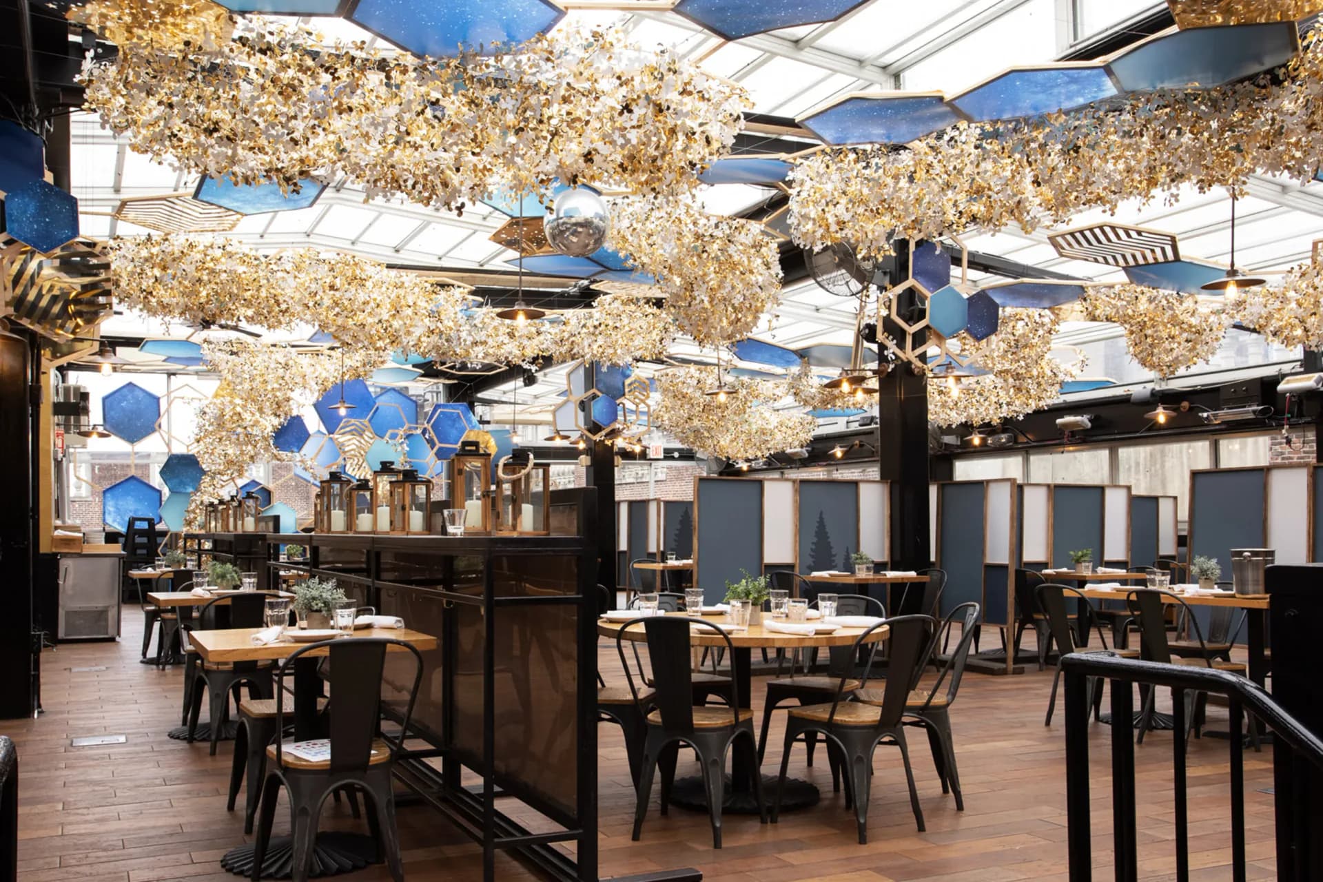 Elegant restaurant interior with gold leaf cloud-shaped ceiling installations, blue pendant accents, wooden tables and black chairs on warm wood flooring by Francesca Signori.