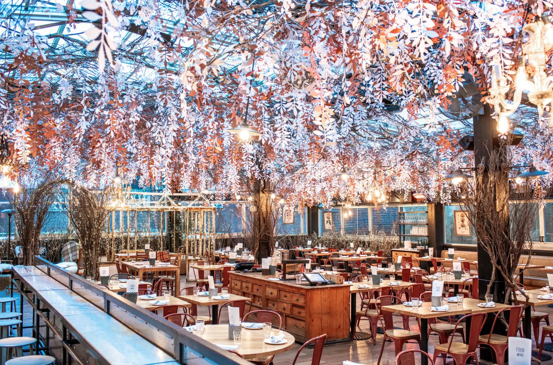 Elegant restaurant interior with soaring wisteria installation overhead, warm wood furnishings, and floor-to-ceiling windows overlooking a city skyline by Francesca Signori.