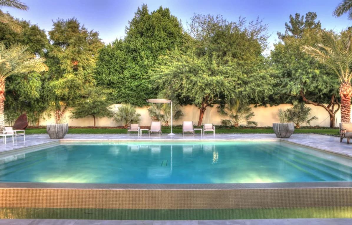 Luxurious rectangular swimming pool with turquoise water surrounded by mature trees, lounge chairs, and manicured landscaping by Frederica Monaco.