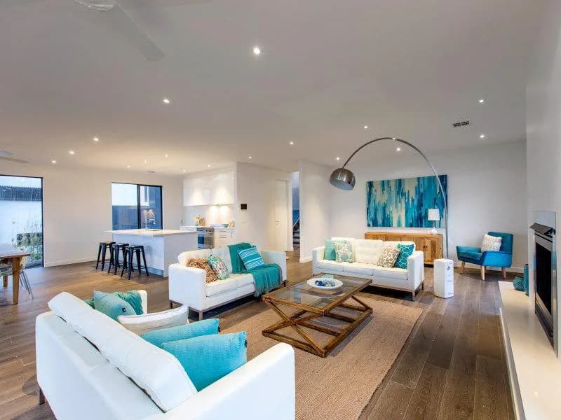 Open-plan living room with white sofas, turquoise accents, wooden flooring, and modern lighting by Frederica Monaco.