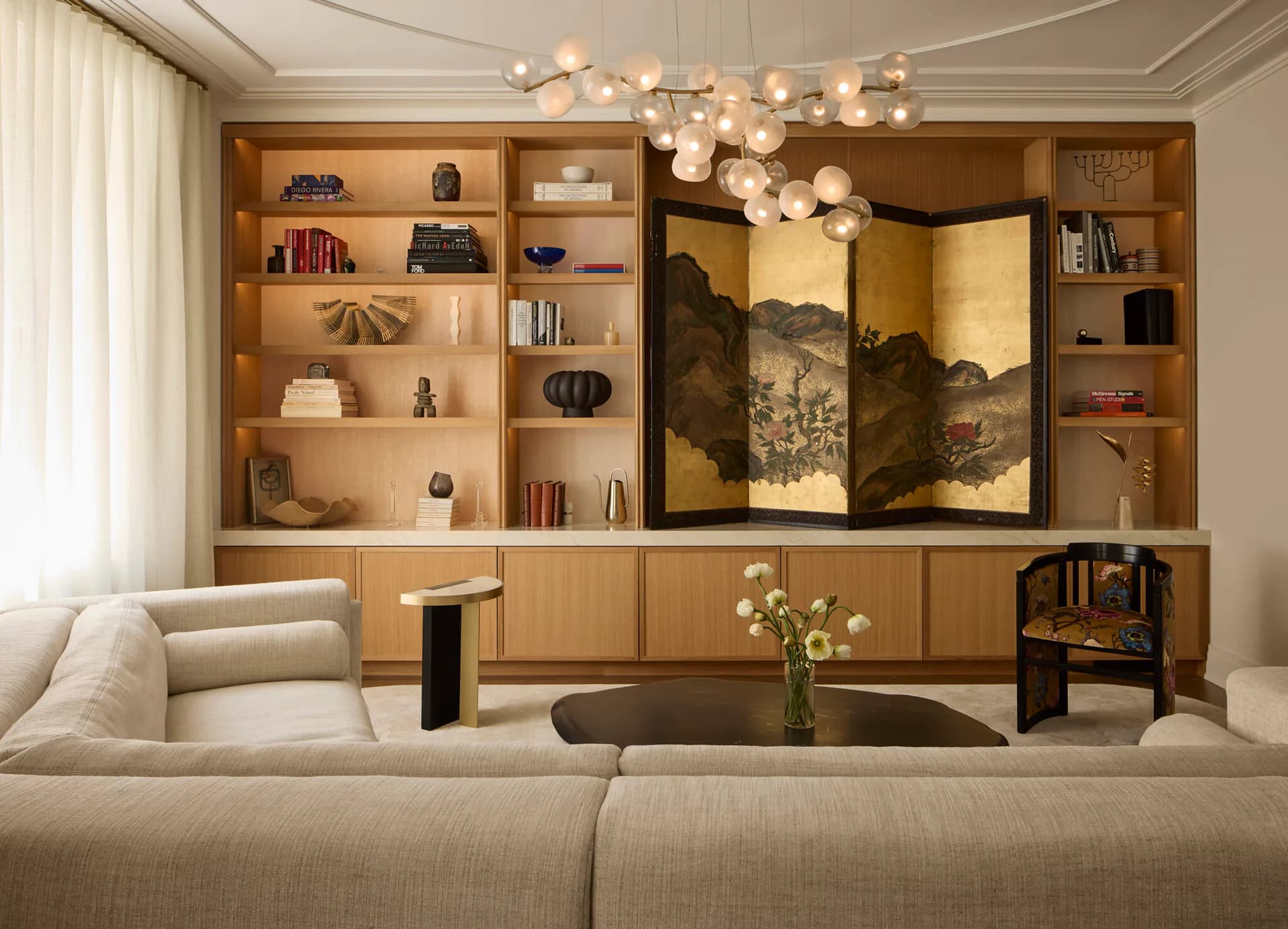 Luxurious living room with warm wood cabinetry, integrated shelving, golden artwork, and modern furnishings designed by Frederick Tang.