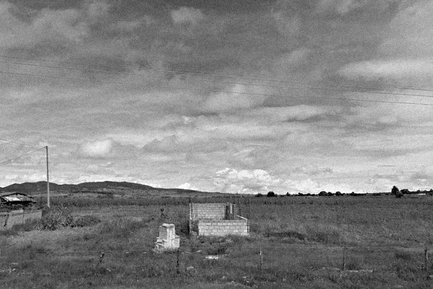 Sparse rural landscape with minimal concrete structures and utility poles under cloudy sky, architectural intervention by Frida Escobedo.