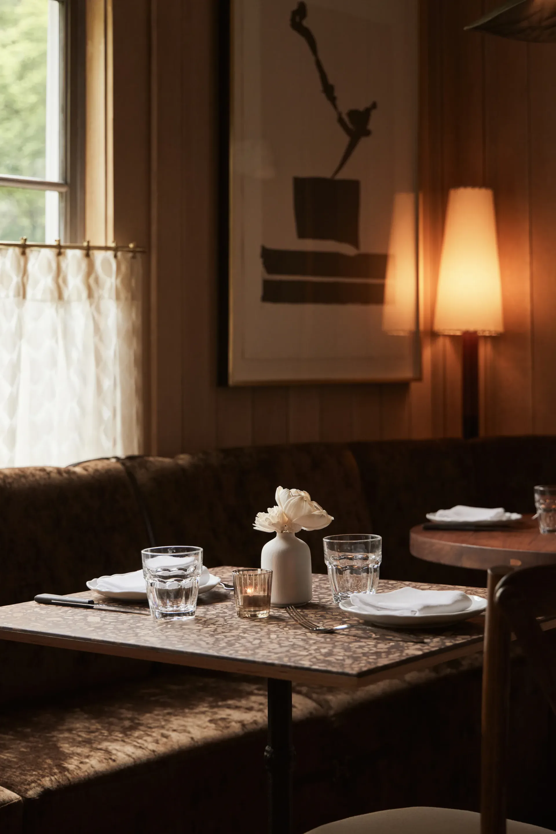 Warm-toned dining room with dark leather seating, marble-topped table set for service, and contemporary artwork on walls by Gabriel Gonzalez.