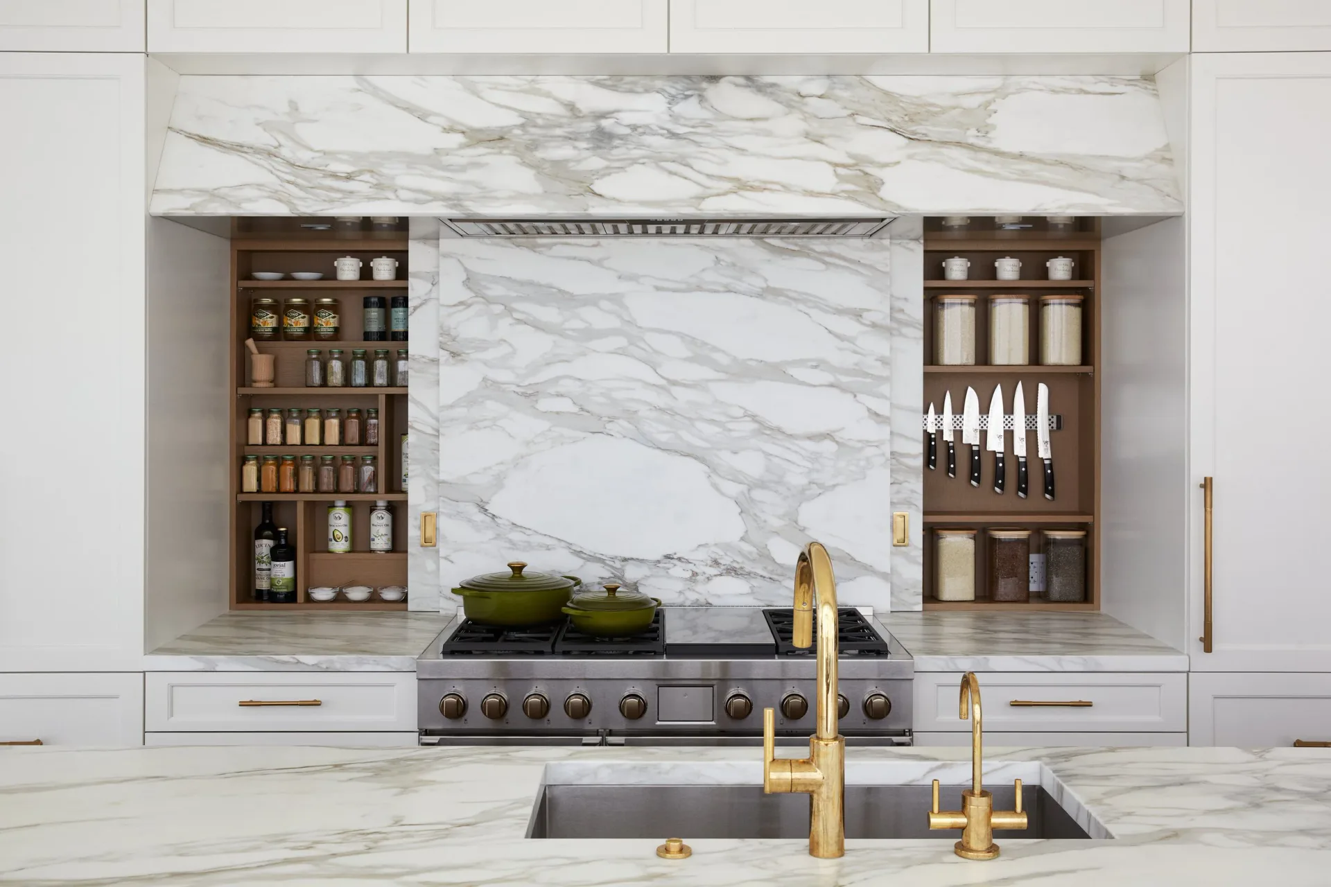 Luxe kitchen with marble backsplash, integrated wood spice shelving, brass fixtures, and waterfall island by Gal Norcross.