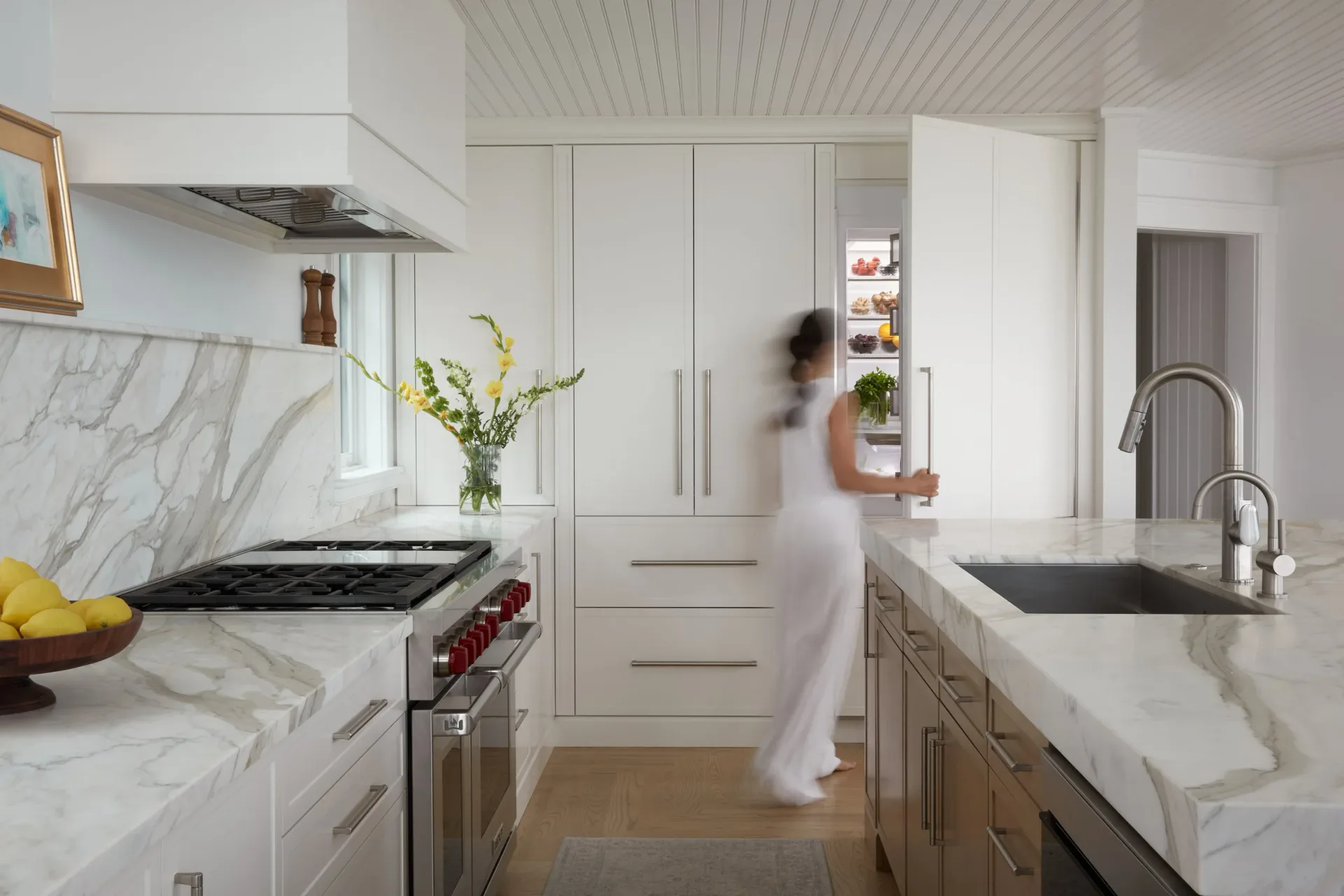 Bright white modern kitchen with marble countertops, white cabinetry, stainless steel appliances, and a large island with prep sink by Gal Norcross.