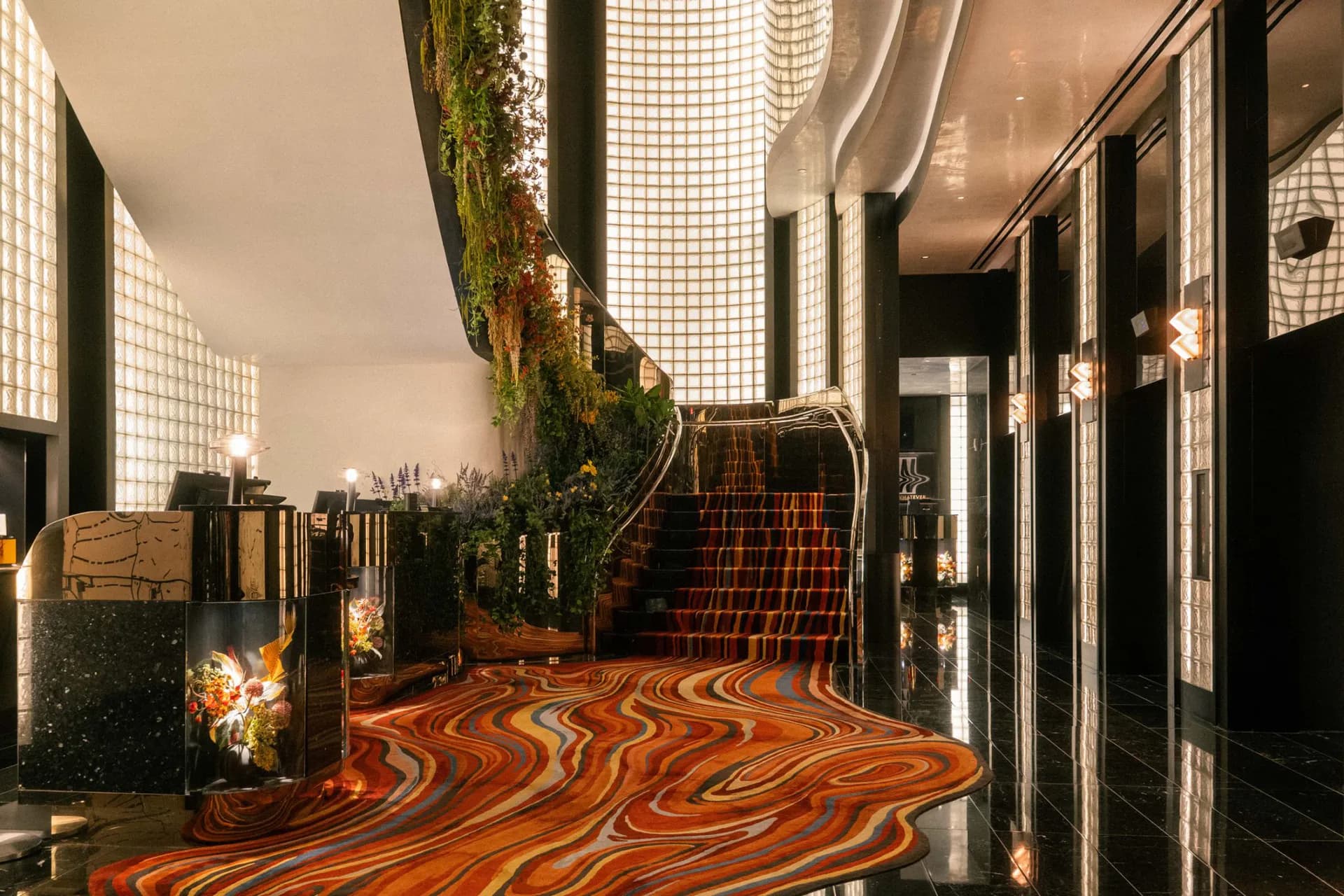 A modern corridor with dramatic orange and black swirled flooring, living moss wall, glass block skylights, and black-framed glass partitions, designed by Gary Wong.