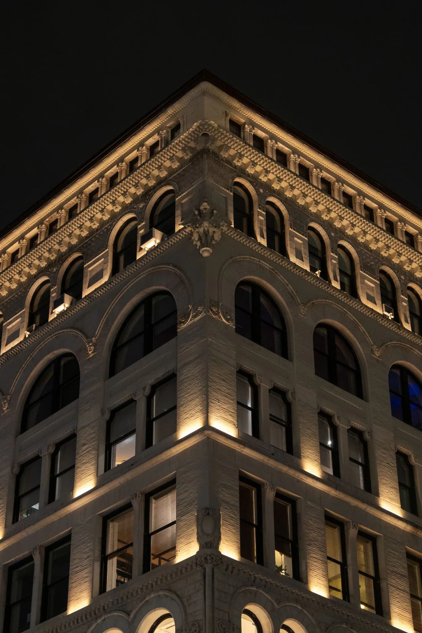 Illuminated historic corner building facade at night showcasing ornate architectural detailing, arched windows, and warm uplighting by Gary Wong.