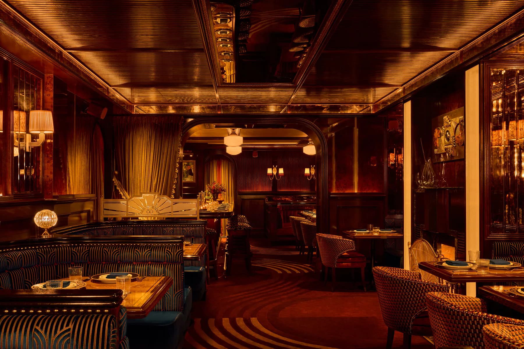 Warm-toned luxury restaurant interior featuring rich wood paneling, ambient golden lighting, striped seating, and dramatic red carpeting by Gary Wong.