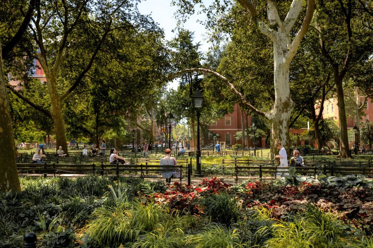 Lush public park with mature trees, vibrant red flowering plants, curved lamp post, and wooden seating areas designed by Gbemi Shonibare.