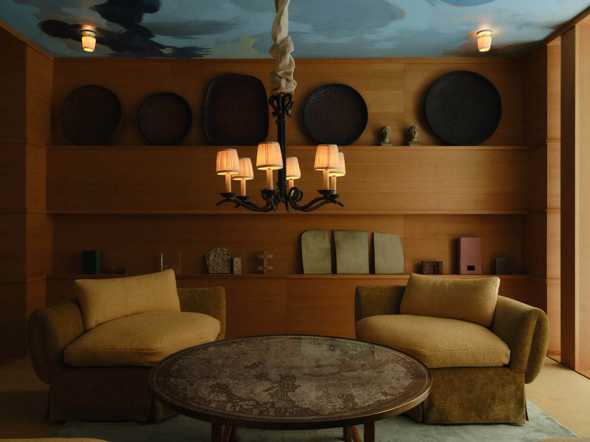 Warm ochre lounge with curved mustard seating, circular stone table, rope chandelier, and decorative wall niches by Giancarlo Valle.