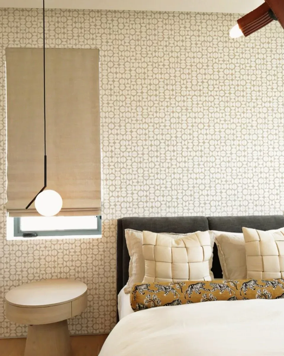 Serene bedroom interior featuring geometric patterned wallpaper, floating pendant light, tailored bedding with decorative pillows, and minimalist side table by Giovanna Fiorello.