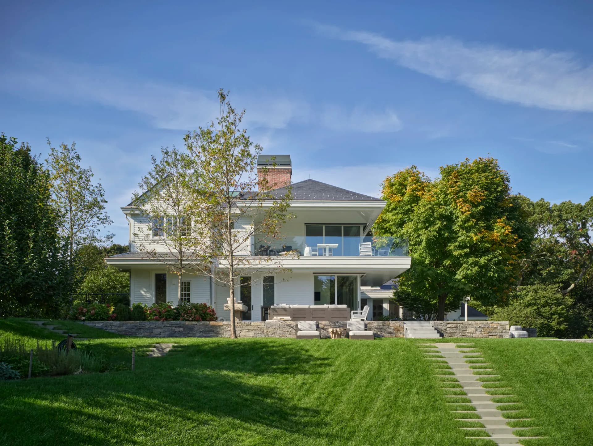 Modern two-story residential home with white exterior, expansive green lawn, stone pathway, and mature landscaping by Gwendolyn Conners.