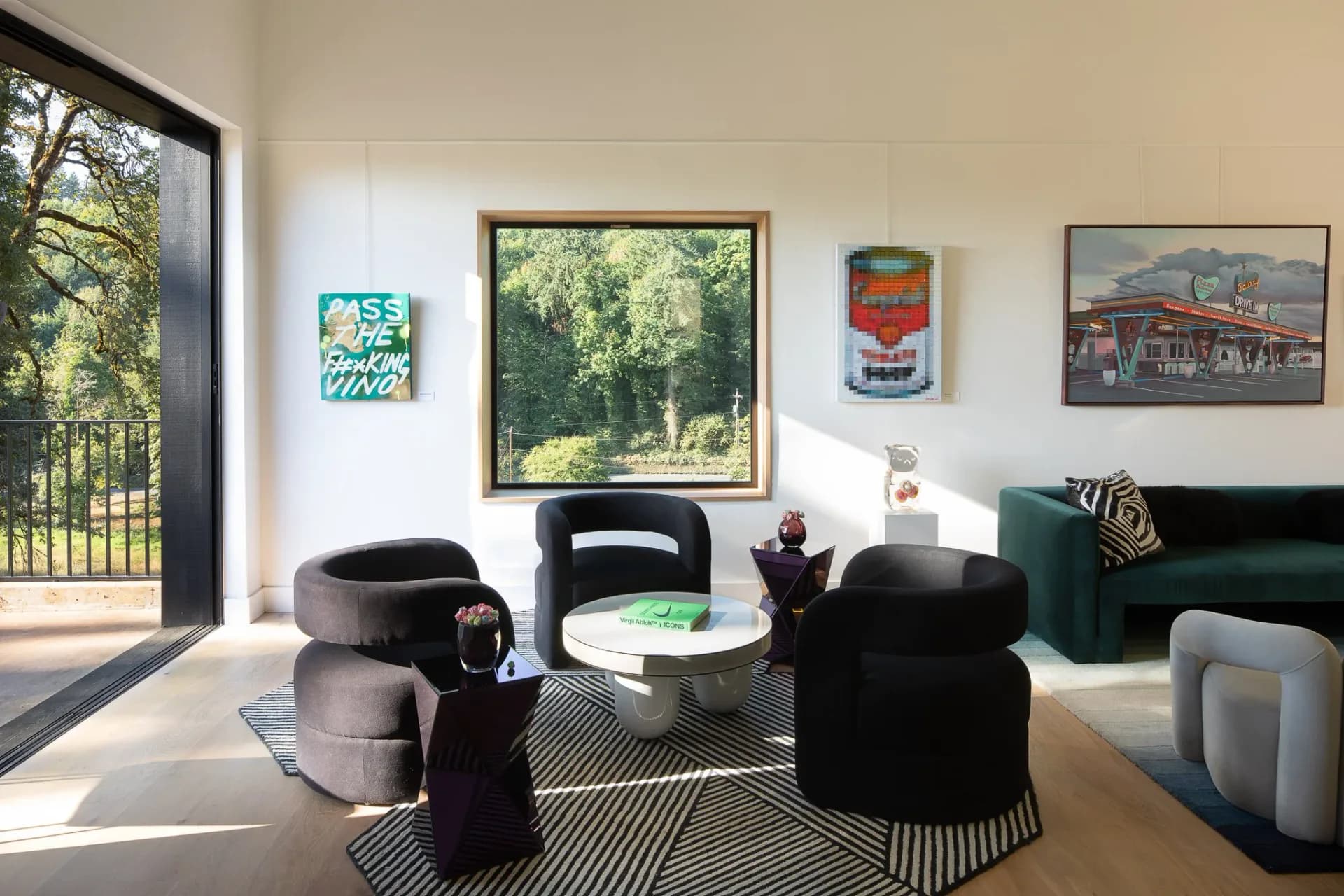 Contemporary living room with curved black and gray upholstered seating, round white table, geometric patterned rug, and large windows overlooking greenery, designed by Hadassah Sweet.