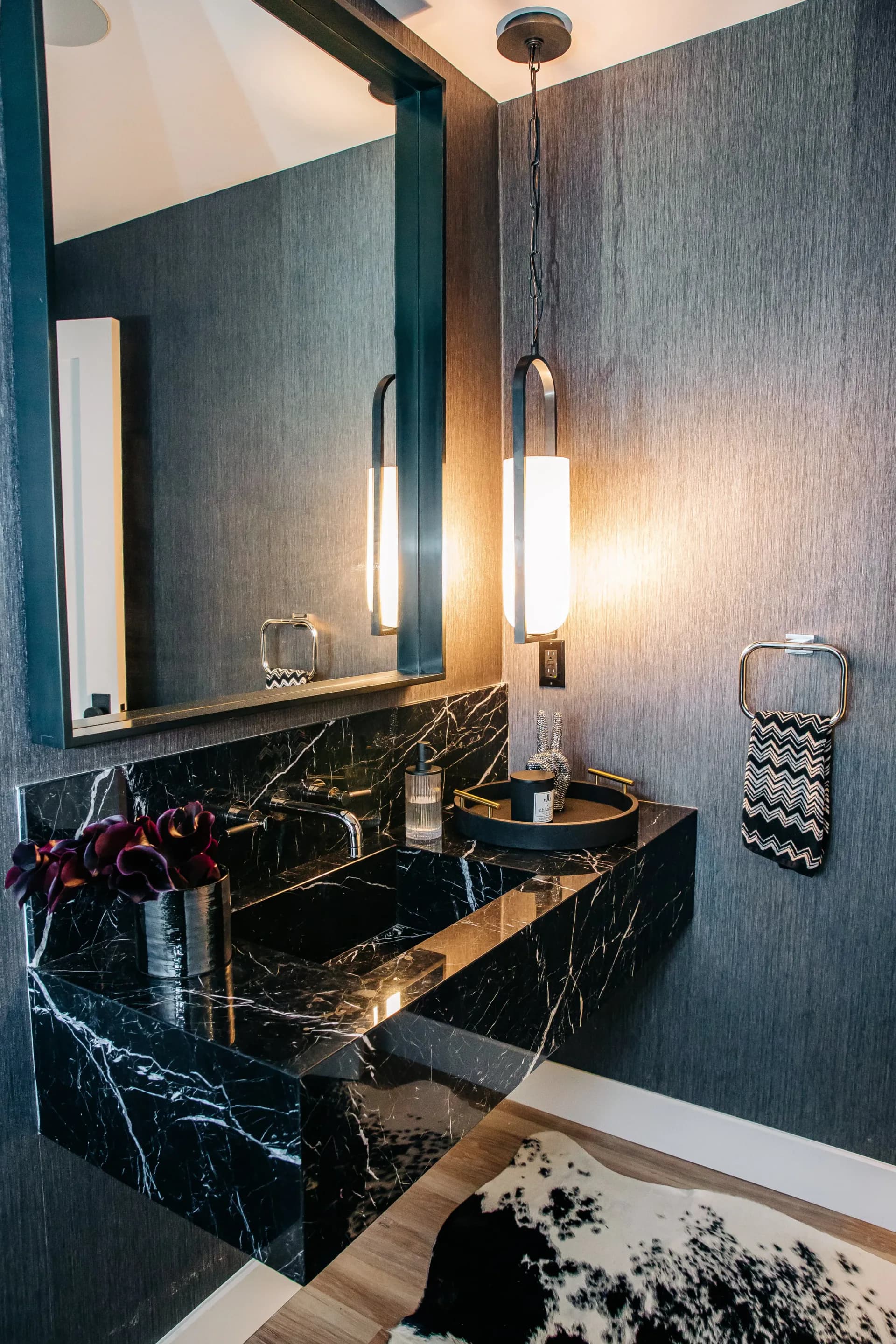 Modern bathroom with black marble vanity, teal textured walls, brass accents, pendant lighting, and large mirror by Hadassah Sweet.