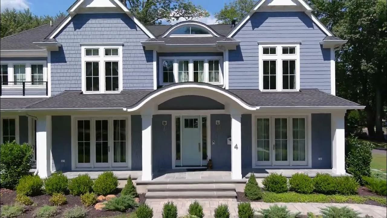 Modern two-story residential home with blue-gray siding, white trim, arched entryway, and manicured landscaping by Haidy Kela.