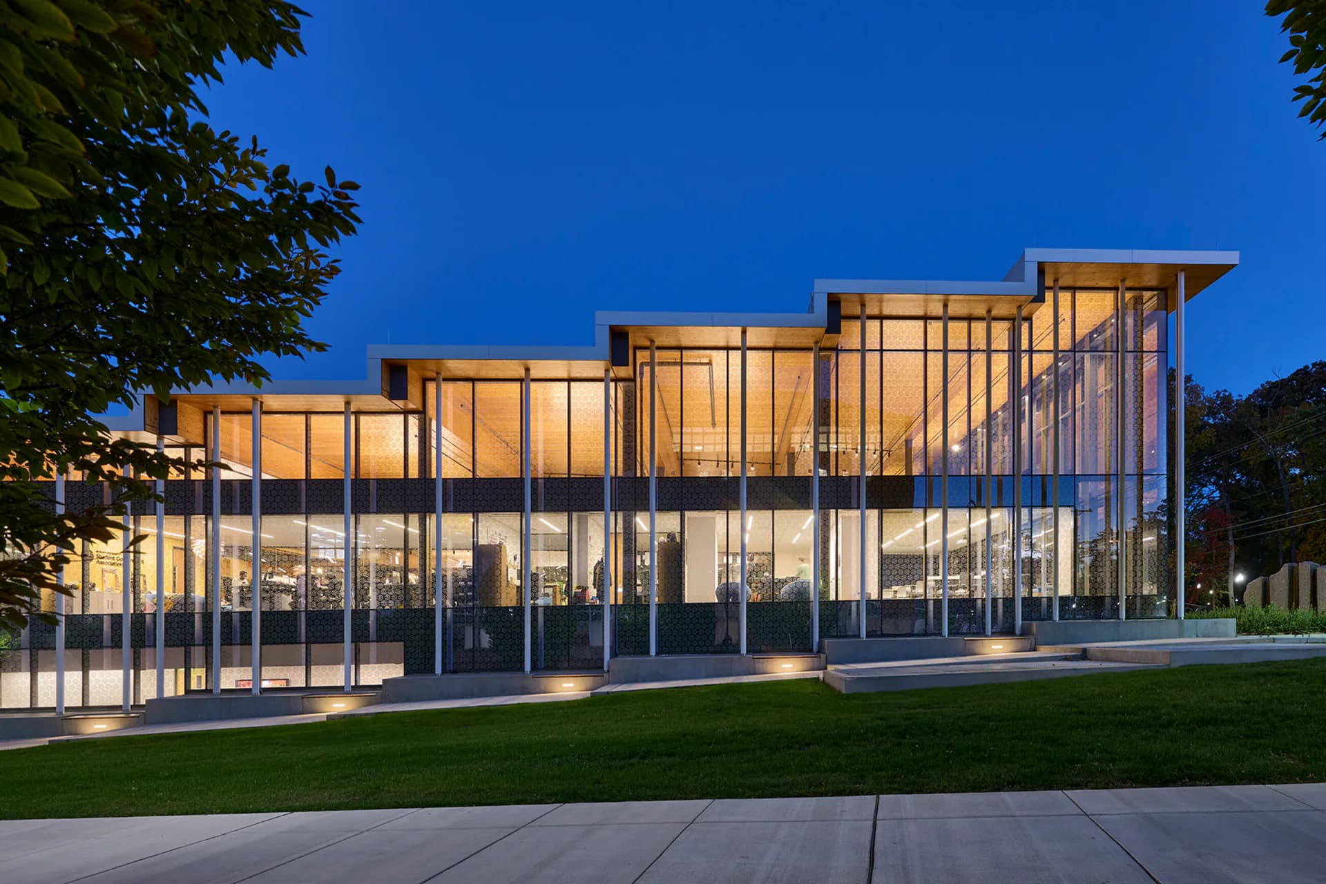 Modern glass-and-metal pavilion with illuminated interior, clean geometric forms, and manicured landscape by Hamilton Guillén.