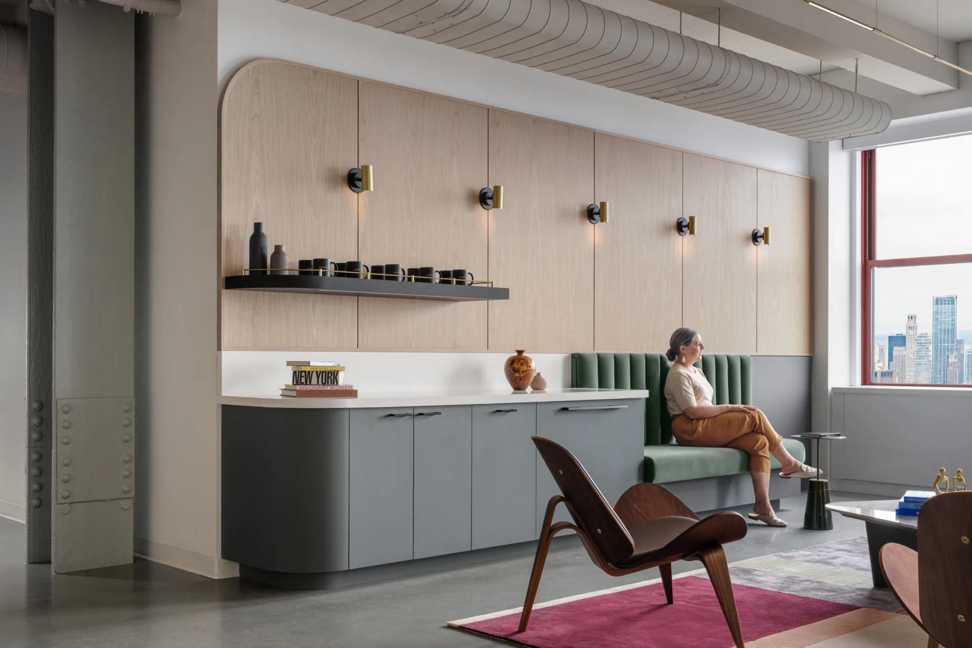 Modern office lounge with light wood cabinetry, dark lower storage, pendant lighting, and green seating by Hamilton Guillén.