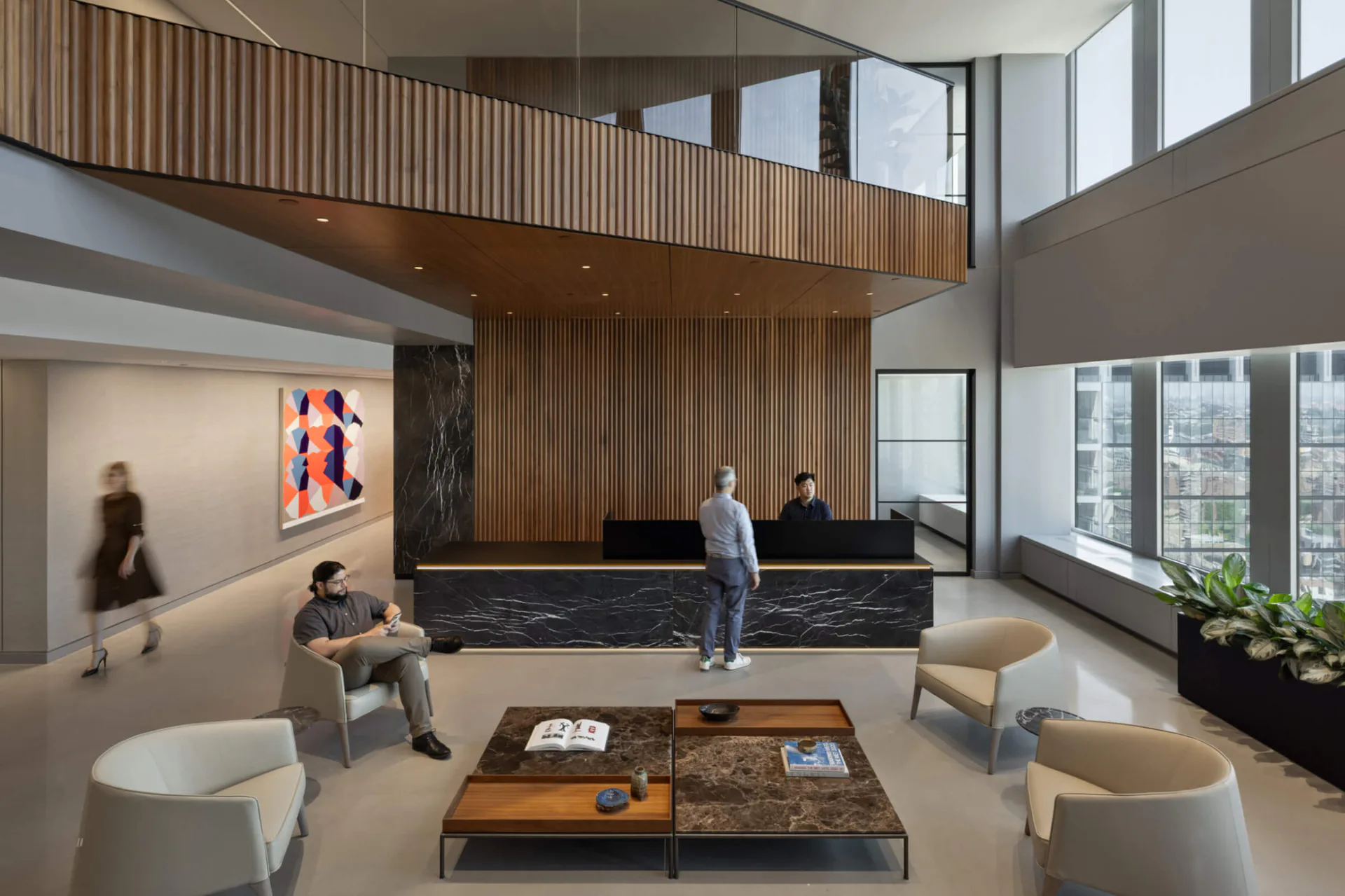 Modern multi-level lobby with wood-slat mezzanine, black terrazzo reception desk, and contemporary seating by Hamilton Guillén.