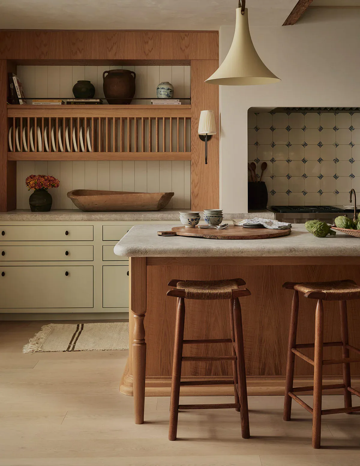 Warm-toned kitchen with cream cabinetry, wood open shelving, and a wood island with seating, featuring a pendant light and tufted backsplash by Hamilton Holmes.