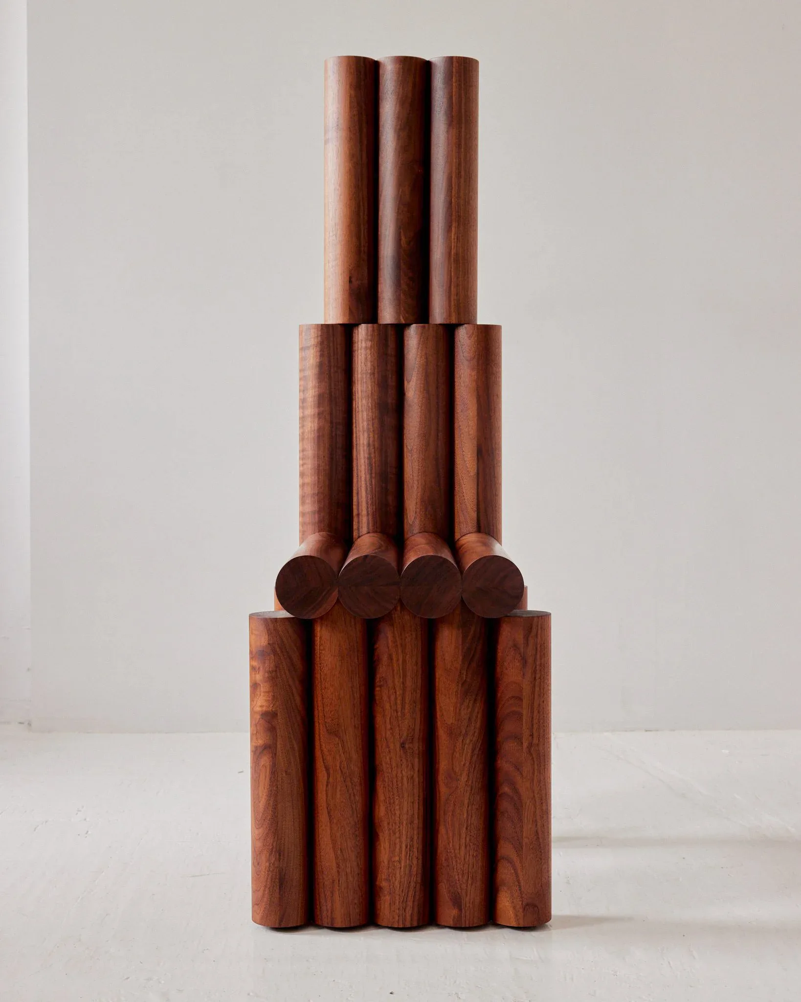 Stacked wooden cylindrical sculpture with tiered composition in warm reddish-brown tones, displayed against neutral background by Hannah Bigeleisen.