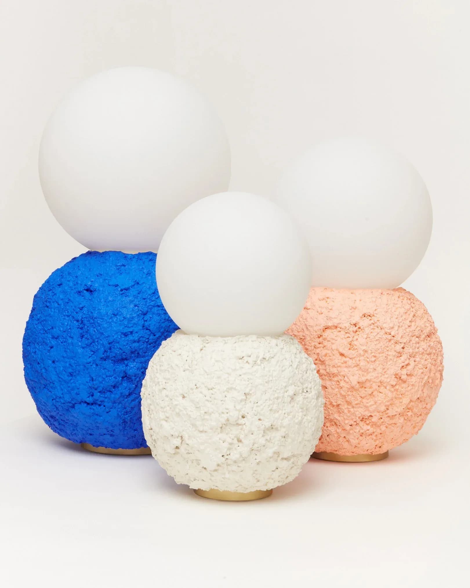 Sculptural bath bomb collection featuring textured spheres in blue, cream, and coral tones with smooth white tops by Hannah Bigeleisen.