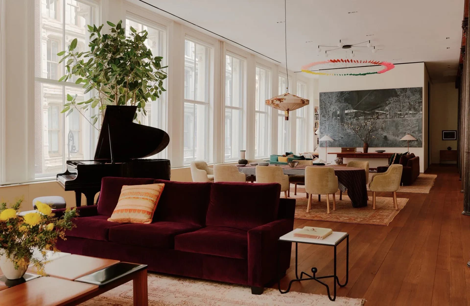 Modern loft interior with burgundy velvet seating, grand piano, wooden dining table, chalkboard wall, and large windows overlooking the city by Hannah McKnight.